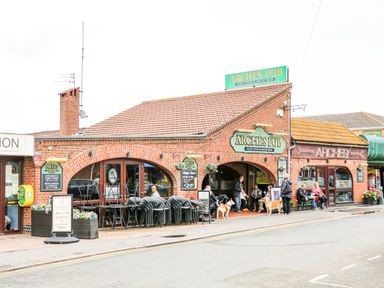 A pub building with arched entrances outdoor seating and people with dogs at 57 Cherry Park in Chapel St Leonards