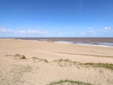 A sandy beach with some grass patches and a person near the water at 57 Cherry Park in Chapel St Leonards