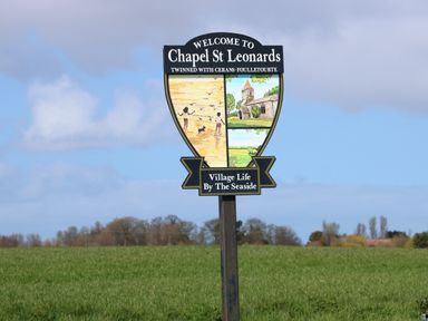 A welcome sign for Chapel St Leonards with illustrations of children on a beach and a church in a grassy field at 57 Cherry Park in Chapel St Leonards