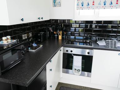 A kitchen with black countertop and backsplash white cabinets microwave oven stove and utensils at 57 Cherry Park in Chapel St Leonards