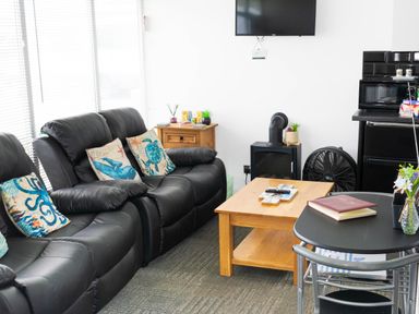 A living room with black leather sofas with sea creature cushions a wooden coffee table a wall-mounted TV a small wooden cabinet and a black table with chairs at 57 Cherry Park in Chapel St Leonards
