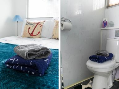 A bed with folded towels on a blue quilt and a pillow with an anchor design next to a toilet with towels on the seat at 57 Cherry Park in Chapel St Leonards