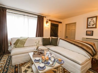 A living room with a white corner sofa and a coffee table set with tea cups and muffins at Norden House in Maiden Newton