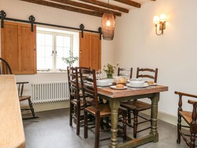 A dining room with a wooden table set for four near a window with wooden shutters at Norden House in Maiden Newton