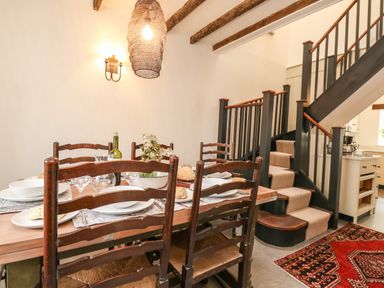 A dining area with a wooden table set with plates and glasses next to a staircase with black railing at Norden House in Maiden Newton