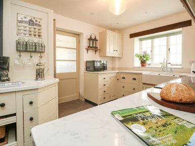 A kitchen with cream cabinets a white countertop a loaf of bread a coffee machine and a window with plants at Norden House in Maiden Newton