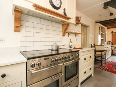 A kitchen with a stainless steel range cooker a pot on the hob white subway tile backsplash and wooden shelves with wine glasses at Norden House in Maiden Newton