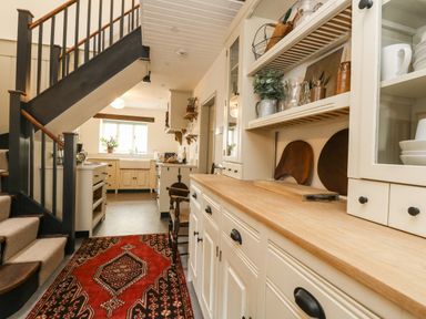 A kitchen with cabinets a wooden countertop a red patterned rug and stairs in Norden House Maiden Newton
