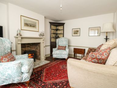 A living room with two patterned armchairs a couch a fireplace and a red rug at Norden House in Maiden Newton