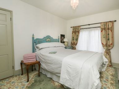 A bedroom with a bed a side table with a lamp a chair with folded towels and curtains at Norden House in Maiden Newton