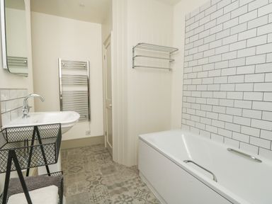 A bathroom with a bathtub tiled wall sink and patterned floor tiles at Norden House in Maiden Newton