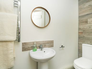 A small bathroom with a round mirror above a pedestal sink with a soap dispenser and a toilet beside it at Norden House in Maiden Newton