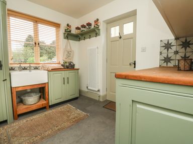 A kitchen with green cabinets a white sink wooden countertop a door and window with blinds at Norden House in Maiden Newton