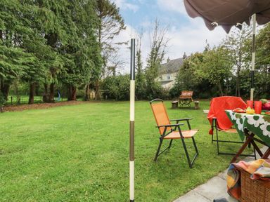 A backyard with chairs a table with an umbrella and a house in the background at Norden House in Maiden Newton