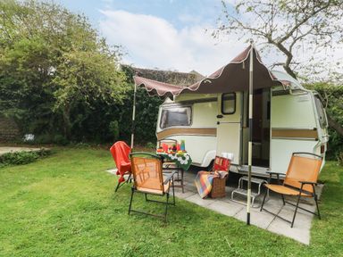 A caravan with an awning set up in a garden with chairs and a table at Norden House Maiden Newton