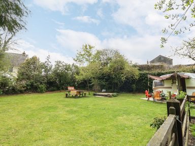 A garden with a picnic table a fire pit and a caravan with outdoor chairs at Norden House in Maiden Newton