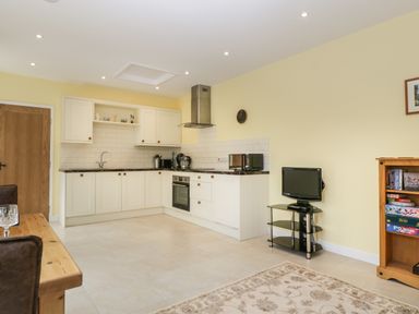 A kitchen with white cabinets and appliances next to a small tv on a stand with a shelf of books at Long Batch Cottage in Ditcheat