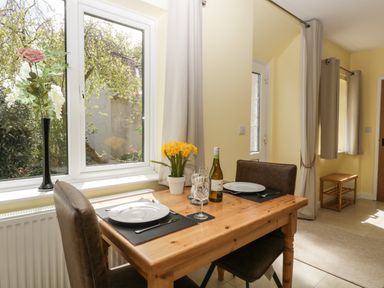 A dining area with a wooden table set for two near a window with flowers on the table at Long Batch Cottage in Ditcheat