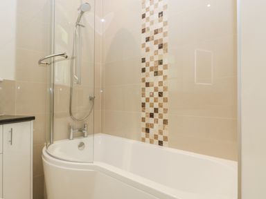 A bathroom with a bathtub shower combination and tiled wall at Long Batch Cottage in Ditcheat