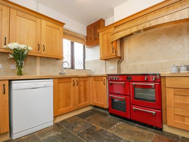 A kitchen with wooden cabinets a red stove a white dishwasher and a vase with flowers at South Boduel Farmhouse in Liskeard