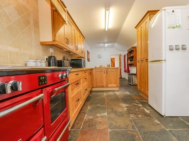 A kitchen with wooden cabinets a red oven a white refrigerator and a tiled floor at South Boduel Farmhouse in Liskeard