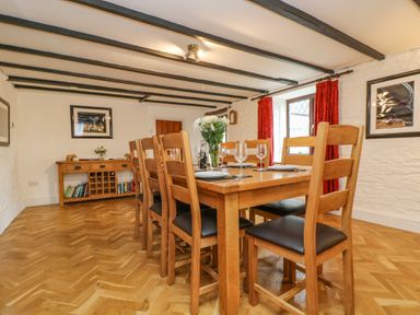 A dining room with a wooden table and chairs set with plates and glasses at South Boduel Farmhouse in Liskeard