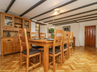 A dining room with a wooden table and eight chairs with a wooden cabinet in the corner at South Boduel Farmhouse in Liskeard