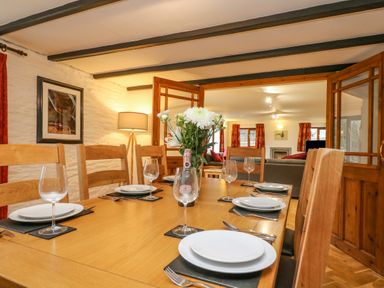 A dining table set with plates wine glasses and cutlery in a room with wooden chairs lamp and artwork at South Boduel Farmhouse in Liskeard