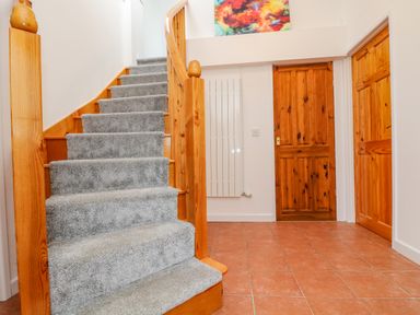 A staircase with gray carpet and wooden railing in a hallway with tiled floor two wooden doors and a colorful painting above a white radiator at South Boduel Farmhouse in Liskeard