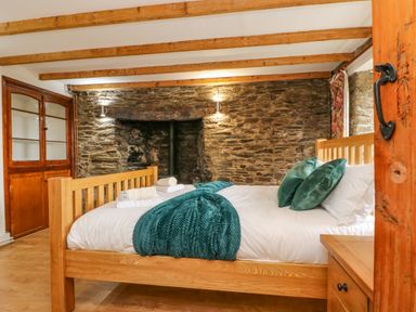 A bedroom with a wooden bed frame and green pillows against a stone wall at South Boduel Farmhouse in Liskeard