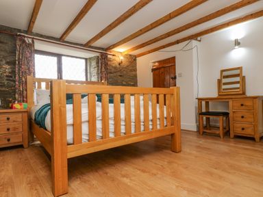 A bedroom with a wooden bed frame a wooden dresser with mirror a wooden nightstand and exposed wooden ceiling beams at South Boduel Farmhouse in Liskeard
