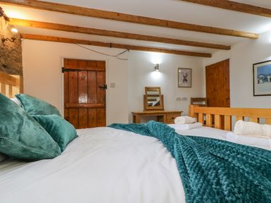 A bedroom with a wooden bed frame green pillows and blanket wooden doors and a dressing table with a mirror at South Boduel Farmhouse in Liskeard
