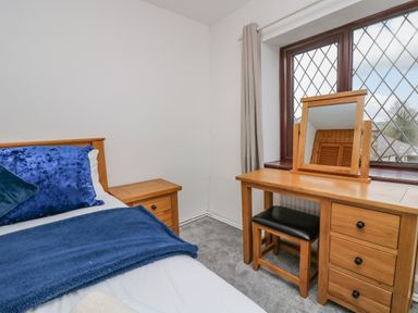 A bedroom with a bed blue pillows and blanket a wooden nightstand and a wooden dressing table with mirror and stool by a window at South Boduel Farmhouse in Liskeard