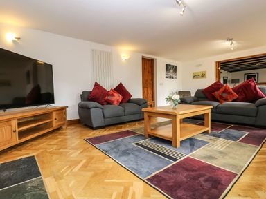 A living room with two gray sofas red and orange cushions a wooden coffee table and a large TV on a wooden stand at South Boduel Farmhouse in Liskeard