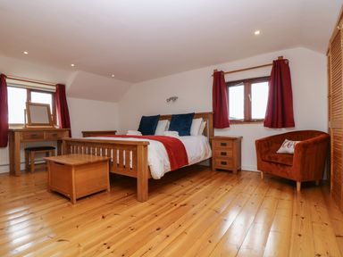 A bedroom with a wooden bed table desk armchair and windows with red curtains at South Boduel Farmhouse in Liskeard