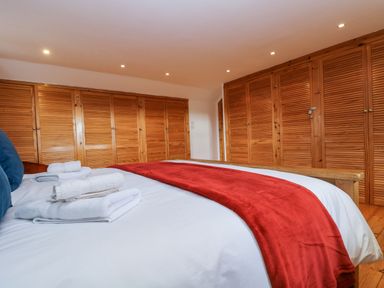 A bedroom with a bed covered in white and red bedding and wooden wardrobes along the walls at South Boduel Farmhouse in Liskeard