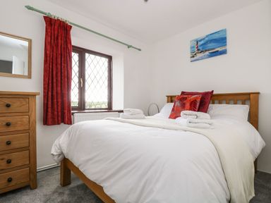A bedroom with a wooden bed and dresser a window with red curtains and a painting above the bed at South Boduel Farmhouse in Liskeard