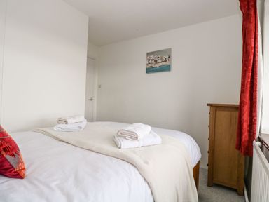 A bedroom with a bed with folded towels on it a wooden dresser a window with red curtains and a painting on the wall at South Boduel Farmhouse in Liskeard