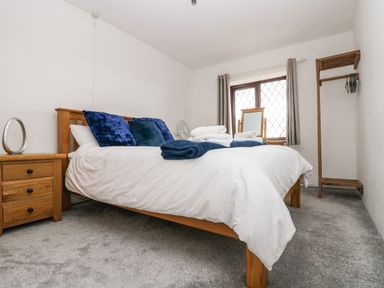 A bedroom with a wooden bed framed with white bedding and blue pillows along with towels on the bed and a wooden nightstand with a small mirror at South Boduel Farmhouse in Liskeard