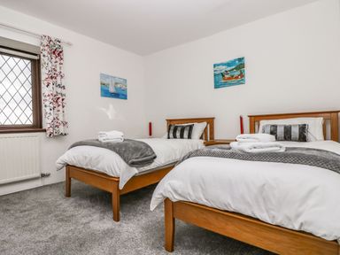 A bedroom with two single wooden beds with white bedding and grey blankets at South Boduel Farmhouse in Liskeard