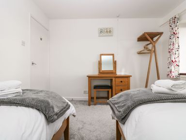 A bedroom with two single beds grey blankets a wooden dressing table and chair and a wooden clothes rack at South Boduel Farmhouse in Liskeard