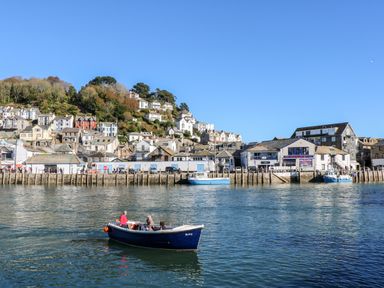 A small boat with people on water near a harbor with buildings and houses on a hillside