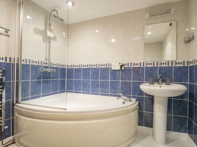 A bathroom with a bathtub shower combination a pedestal sink a mirror and tiled walls at South Boduel Farmhouse in Liskeard