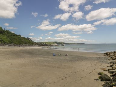A sandy beach with scattered rocks kayaks and people by the water near green hills and a distant coastline