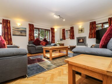 A living room with gray sofas red cushions a wooden coffee table fireplace and patterned curtains at South Boduel Farmhouse in Liskeard