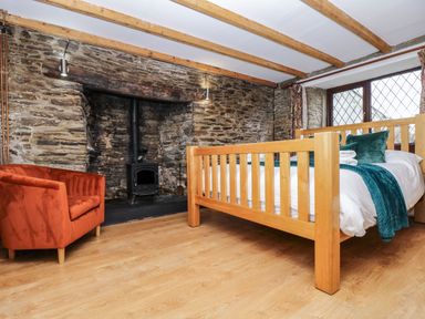 A bedroom with a wooden bed a fireplace with a wood stove and an orange armchair at South Boduel Farmhouse in Liskeard