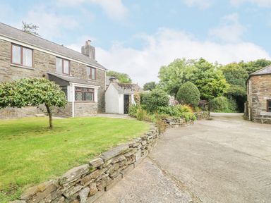 An exterior view of a stone farmhouse with a small leaning tree and raised garden bed on a lawn at South Boduel Farmhouse in Liskeard