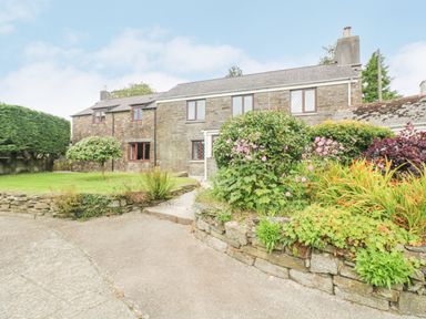A stone farmhouse with a garden and flower beds in front at South Boduel Farmhouse in Liskeard
