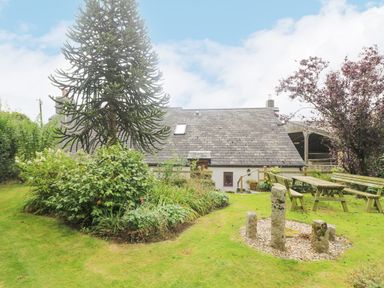 A garden with a large tree a flower bed stone pillars and wooden benches at South Boduel Farmhouse in Liskeard