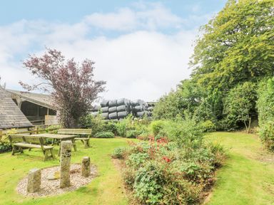 A garden with a wooden picnic table and benches stone sculpture plants and trees at South Boduel Farmhouse in Liskeard